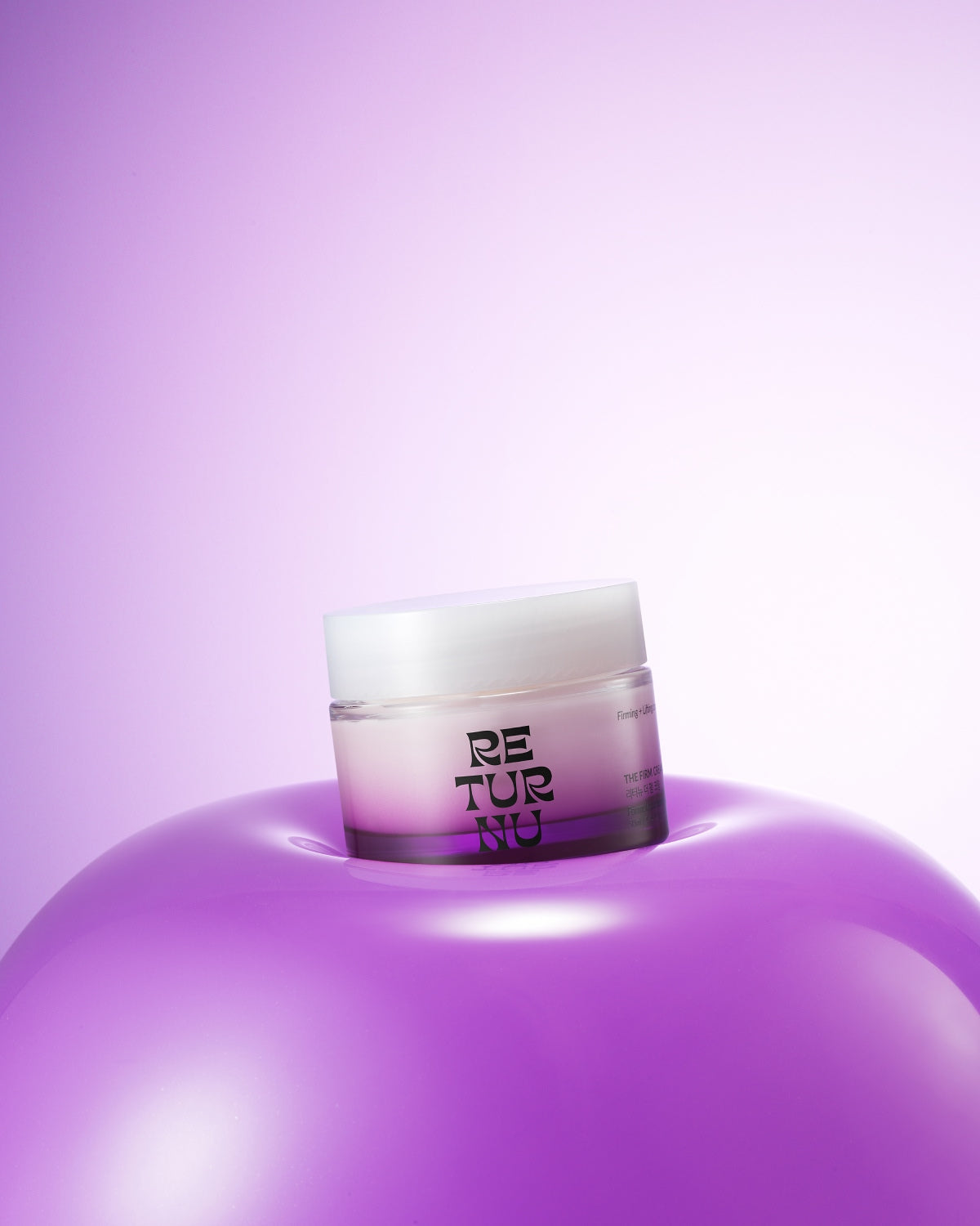 The purple gradient cream jar resting in the center of a large, glossy purple sphere against a light purple background.