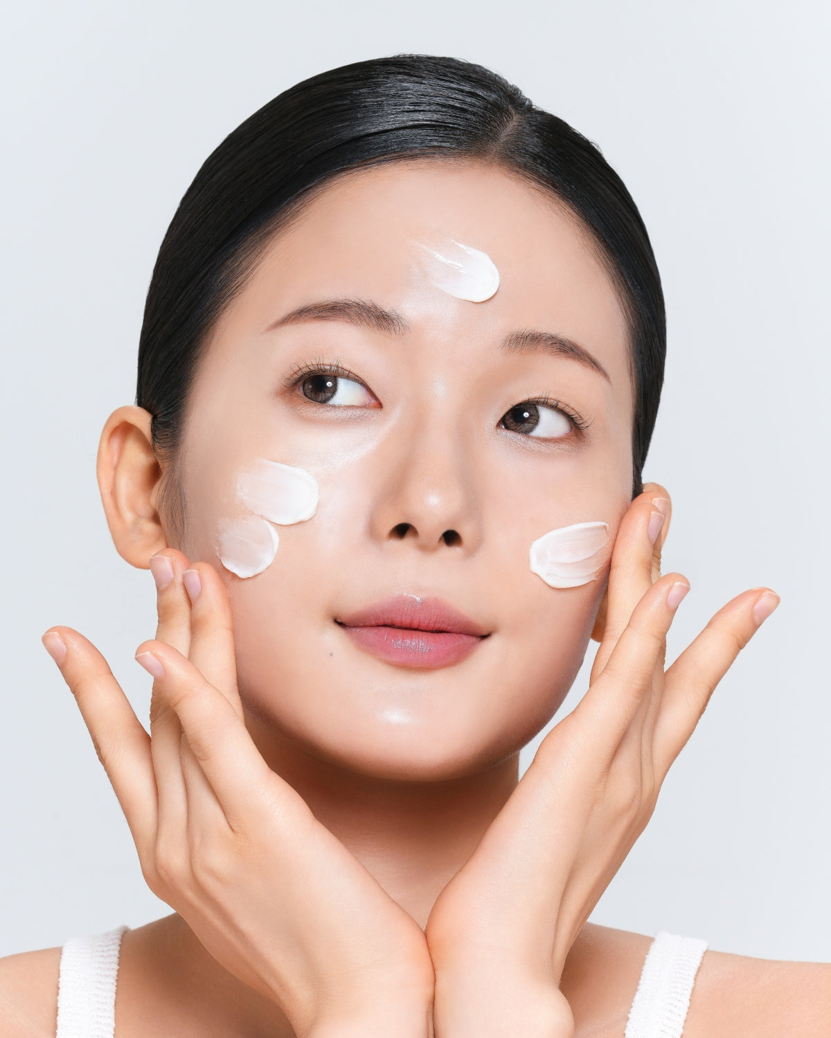 A person looking slightly upward with several small swipes of white cream applied to their forehead and cheeks.