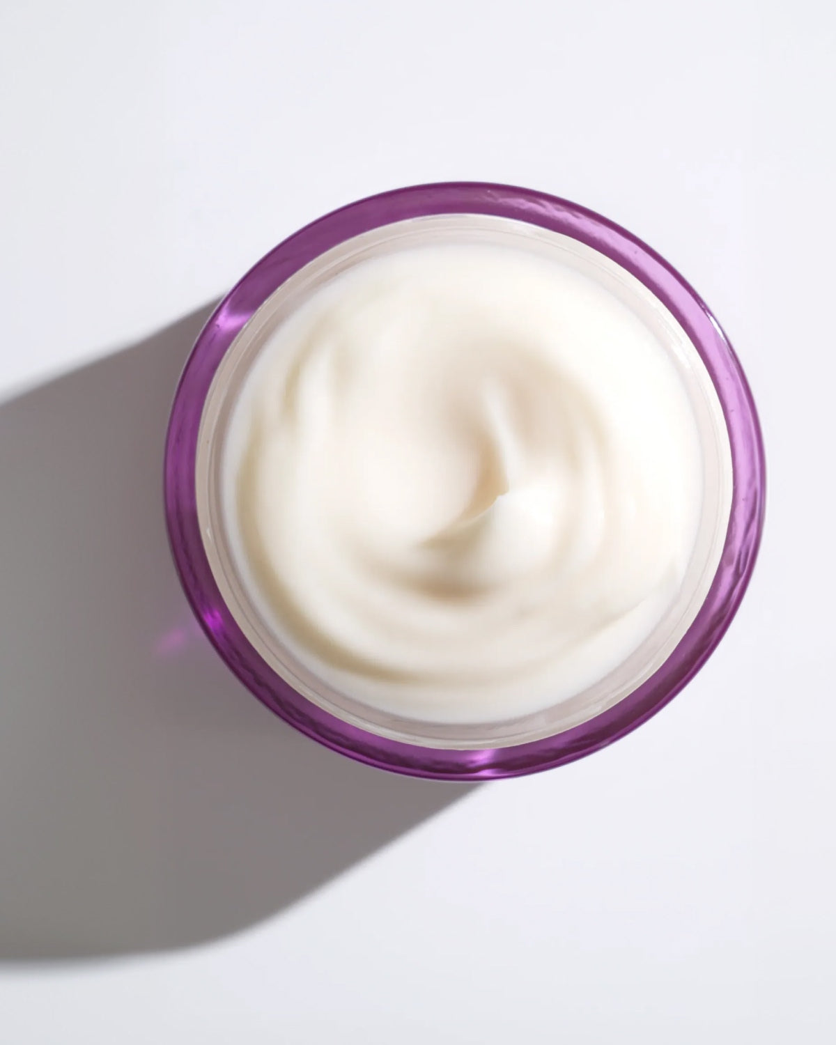 A top-down view of an open purple jar filled with smooth, thick white cream.