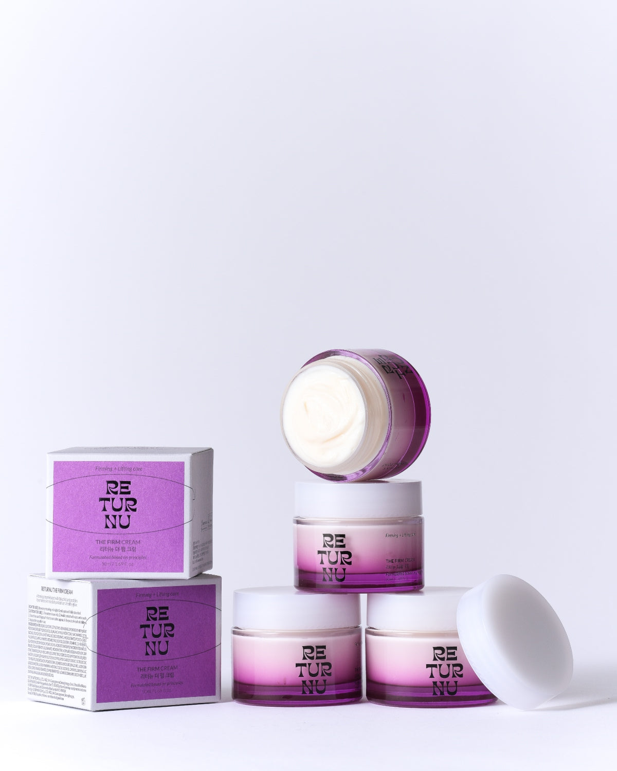 A collection of cream jars and their purple cardboard packaging stacked in a pyramid arrangement on a white surface.