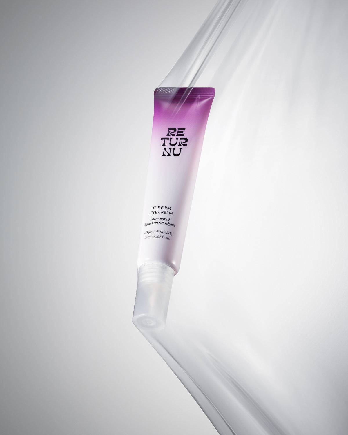 The eye cream tube positioned vertically behind a transparent, draped plastic film on a grey and white background.