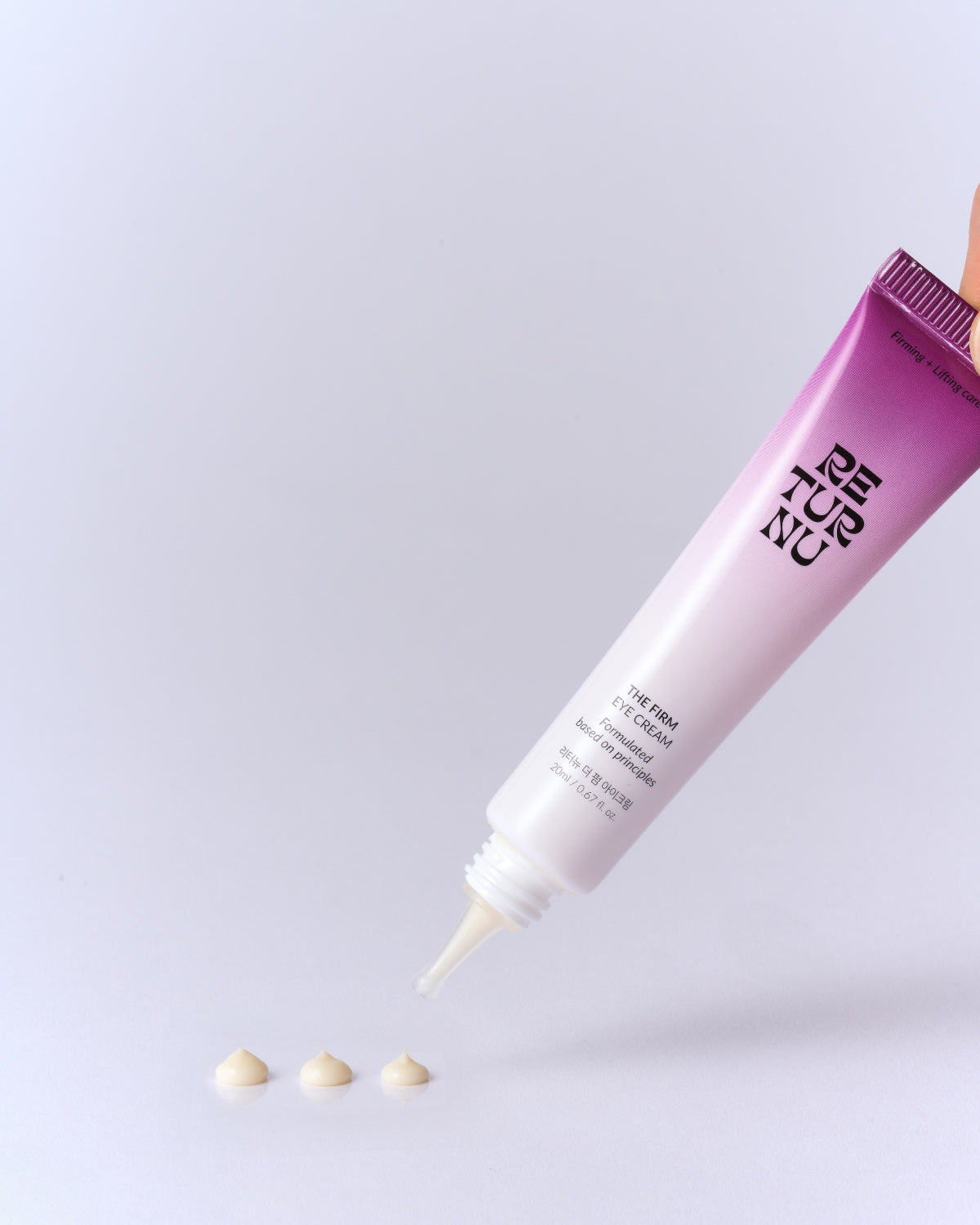 The eye cream tube being held at an angle, dispensing three small, uniform dots of cream onto a white surface.