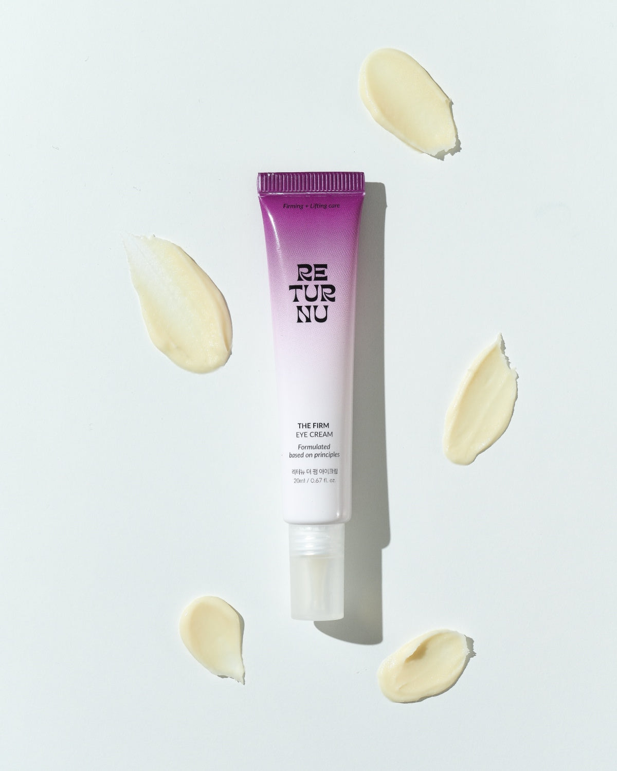 A top-down view of the eye cream tube surrounded by five decorative smears of thick, light-yellow cream on a white background.