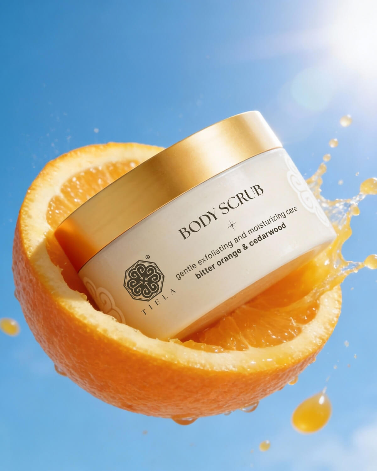 A jar of Tiela Bitter Orange & Cedarwood scrub nestled inside a halved orange with juice splashing around it.