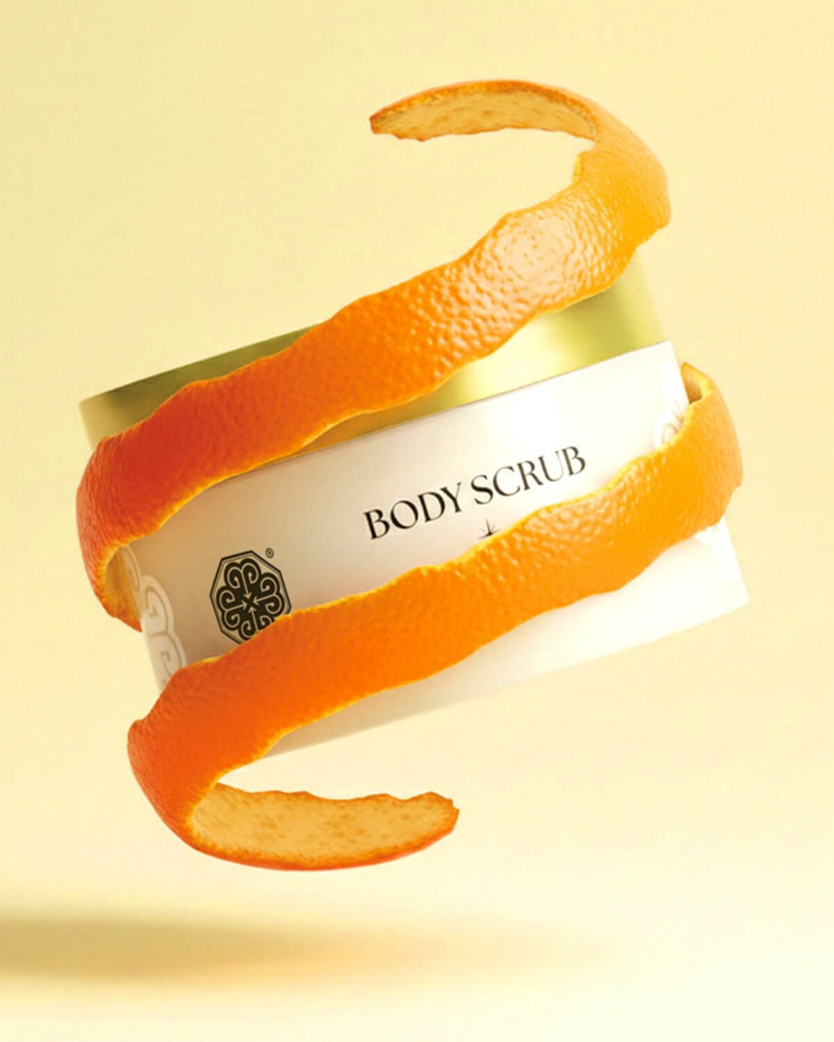 A jar of Tiela Bitter Orange & Cedarwood body scrub wrapped in a spiraling orange peel against a yellow background.