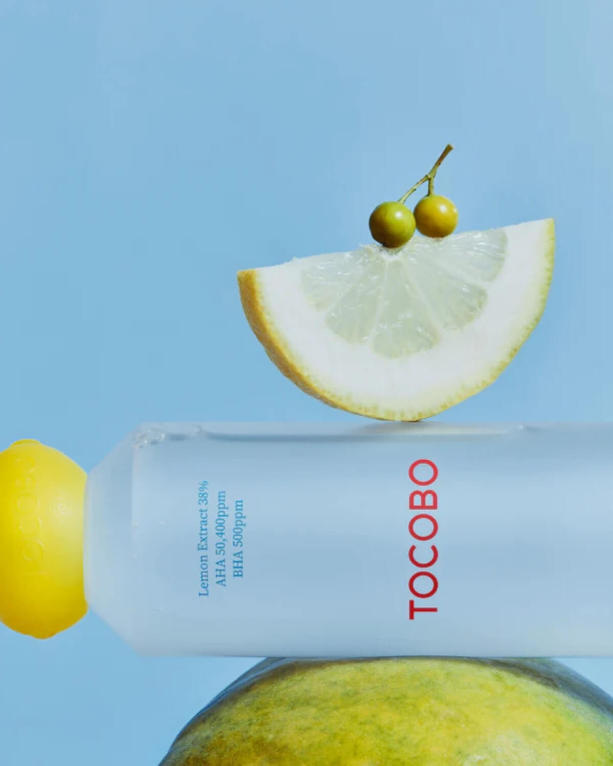 Aesthetic shot of Tocobo Lemon Toner bottle with a fresh lemon slice and small citrus fruits on a blue background.