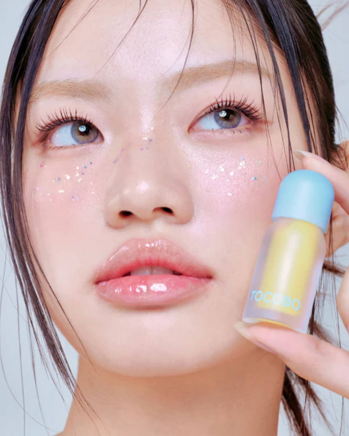 Model with glitter makeup wearing clear glossy Tocobo Honey Lemon lip oil for a high-shine finish.