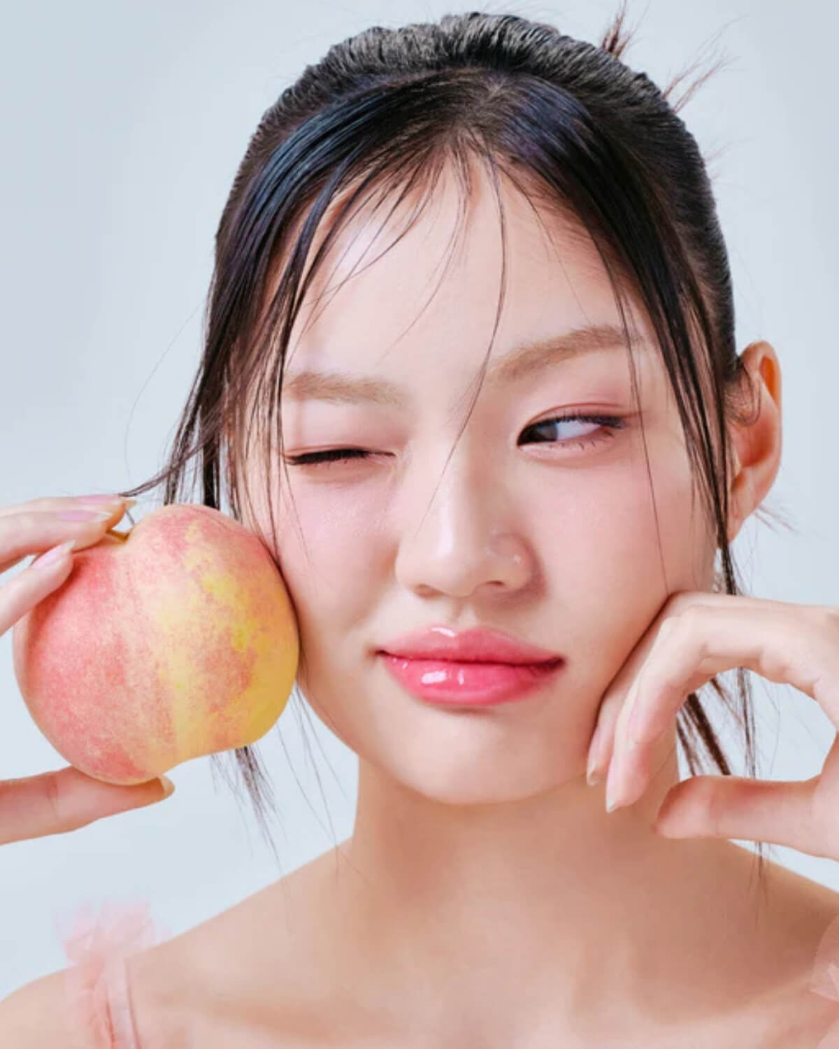Model wearing pink Tocobo lip oil posing with a peach to showcase a juicy, hydrated lip look.