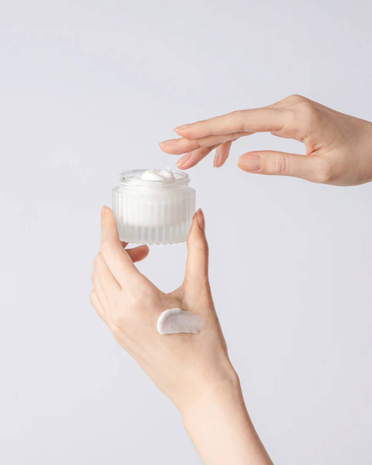 Hands holding an open jar of Tocobo Multi Ceramide Cream with a small swatch applied to the back of the hand.