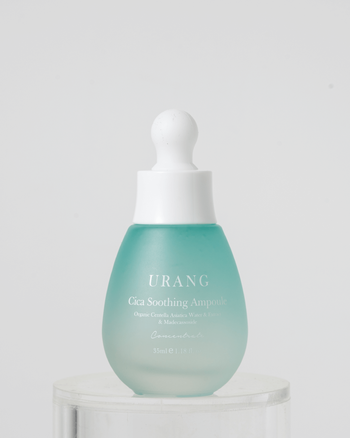 Urang Cica Soothing Ampoule bottle with a light green tint on a clear pedestal, highlighting the soothing and repairing power of organic Centella asiatica.