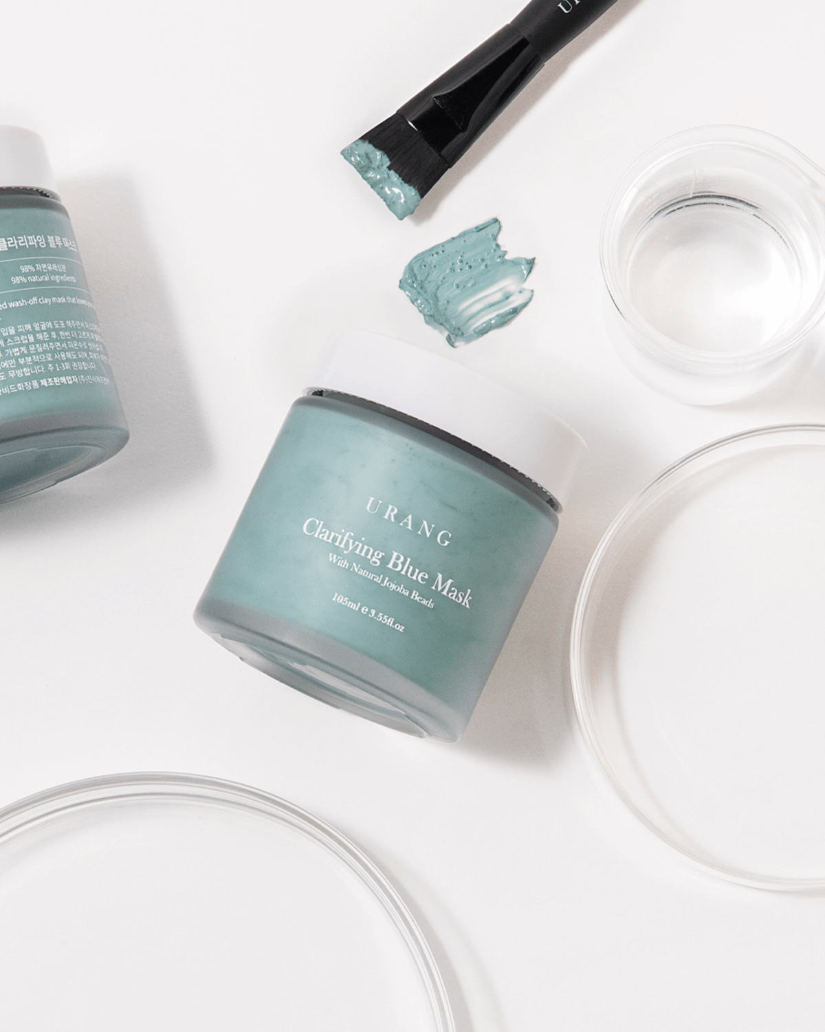 Urang Clarifying Blue Mask jar open, with a swatch and brush nearby, illustrating the soft, easily spreading clay texture for gentle exfoliation and clarification.