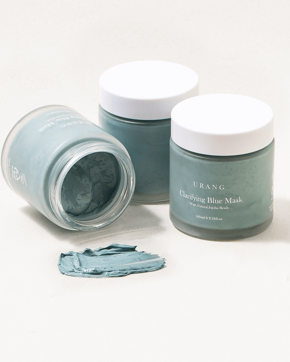 Three jars of Urang Clarifying Blue Mask, with a smear showing the creamy blue clay texture that gently exfoliates and clarifies dull skin.