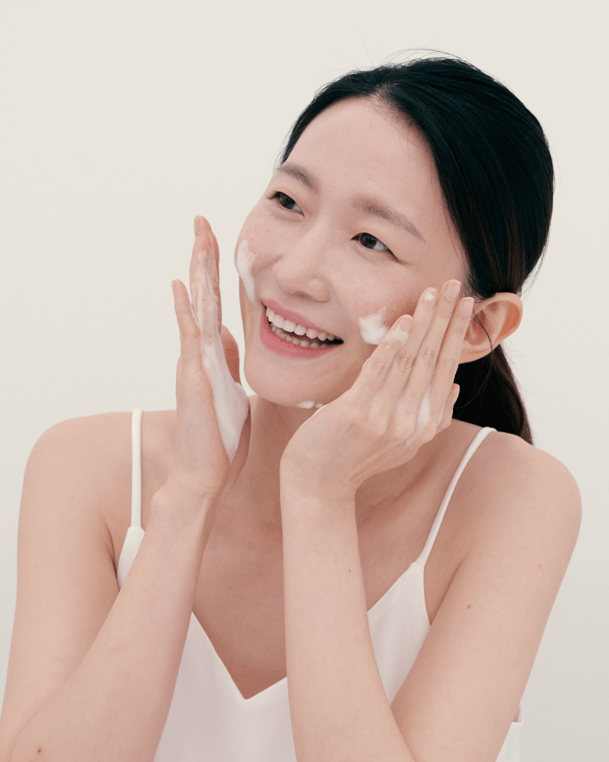Smiling woman gently massaging Urang Creamy Bubble Foam Cleanser onto her face, showing the soothing foam texture ideal for sensitive and easily irritated skin.
