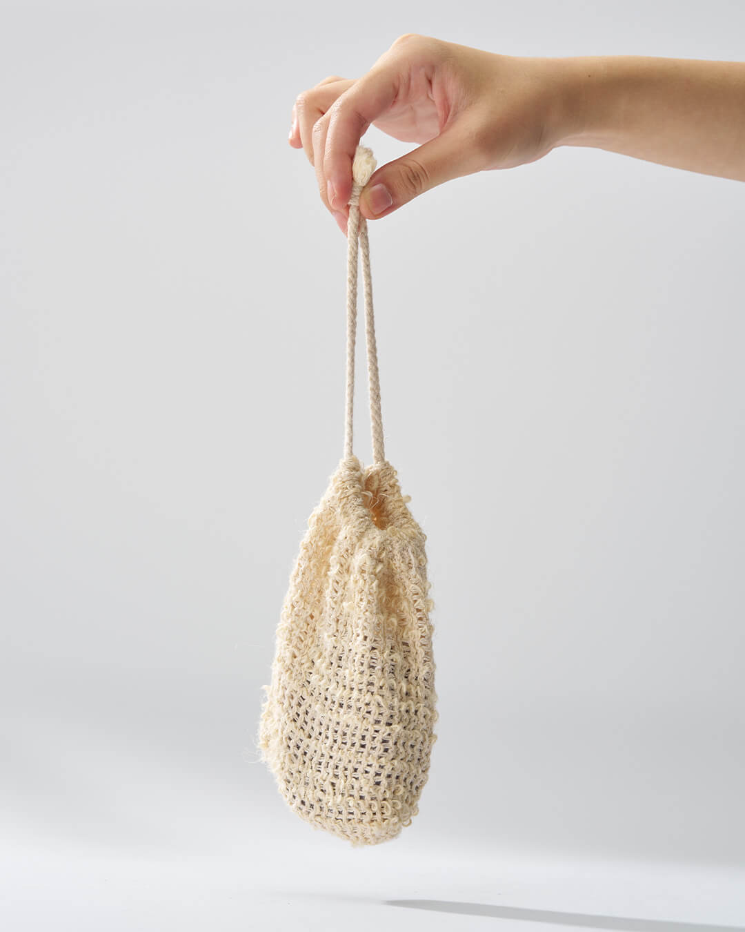 Hand holding a solid Urang Daily Oil Control Shampoo Bar inside a textured, woven drawstring pouch (or foaming net).