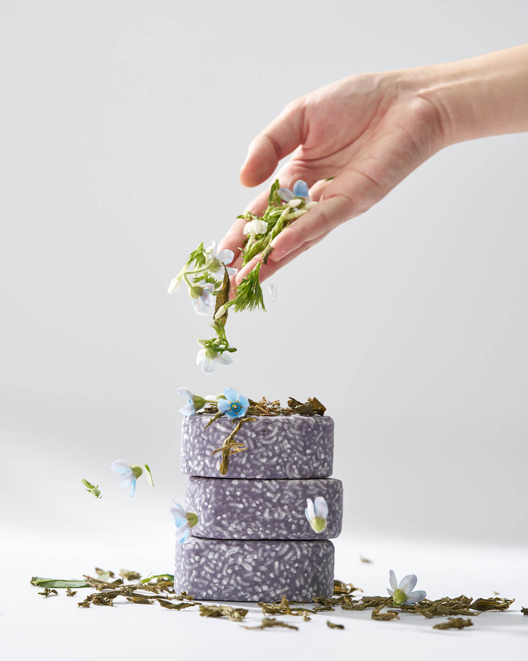 Three stacked Urang Daily Oil Control Shampoo Bars, decorated with flowers and green tea leaves, symbolizing the natural ingredients that clarify and balance the oily scalp.