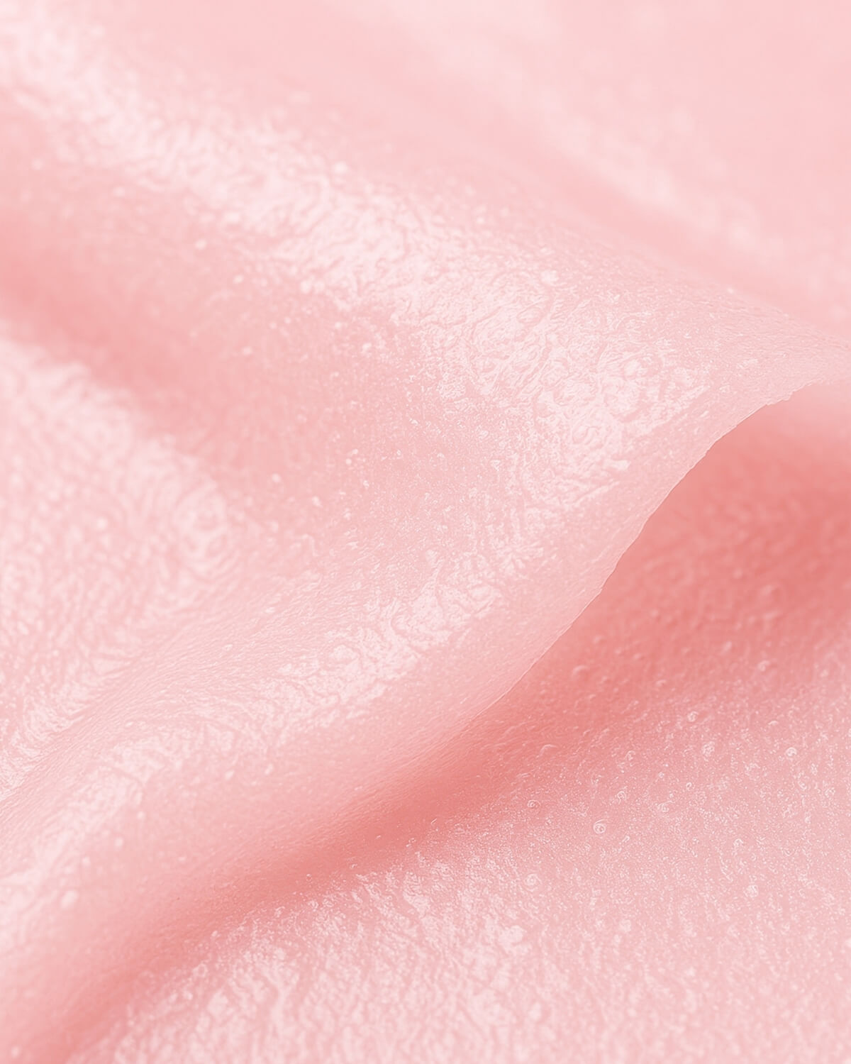 Extreme close-up of the wrinkled, pink, semi-transparent sheet mask material, showing its texture.