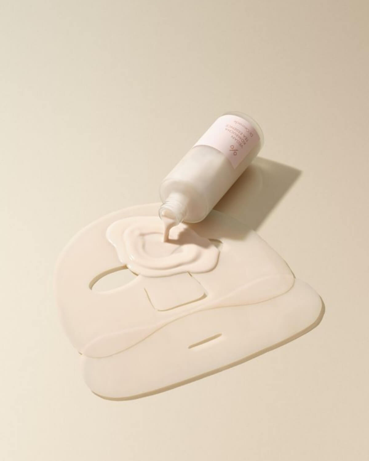 Dr. Ceuracle Vegan Kombucha Tea Essence pouring onto a hydrogel sheet mask to show the creamy, nutrient-rich formula.