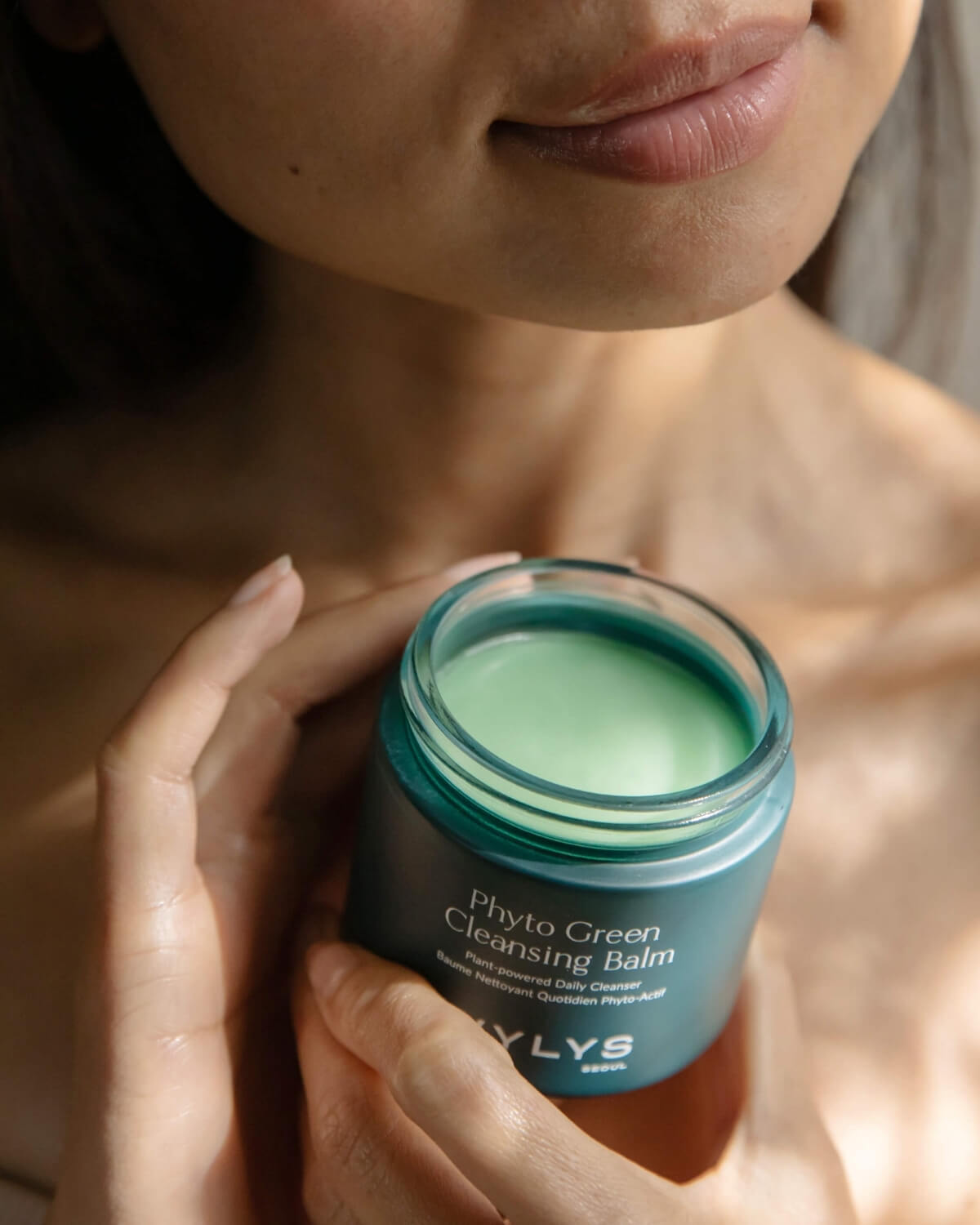 A person holding an open jar of WYLYS Phyto Green Cleansing Balm, highlighting the plant-powered green formula.