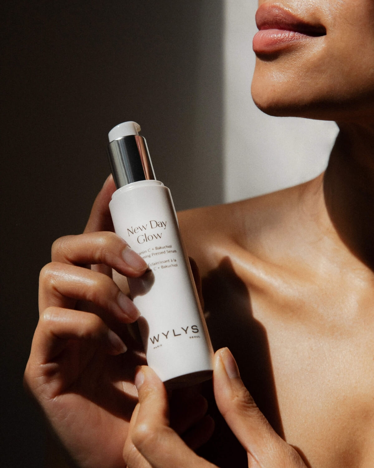 A woman holding the WYLYS New Day Glow Vitamin C + Bakuchiol Brightening Pressed Serum pump bottle.