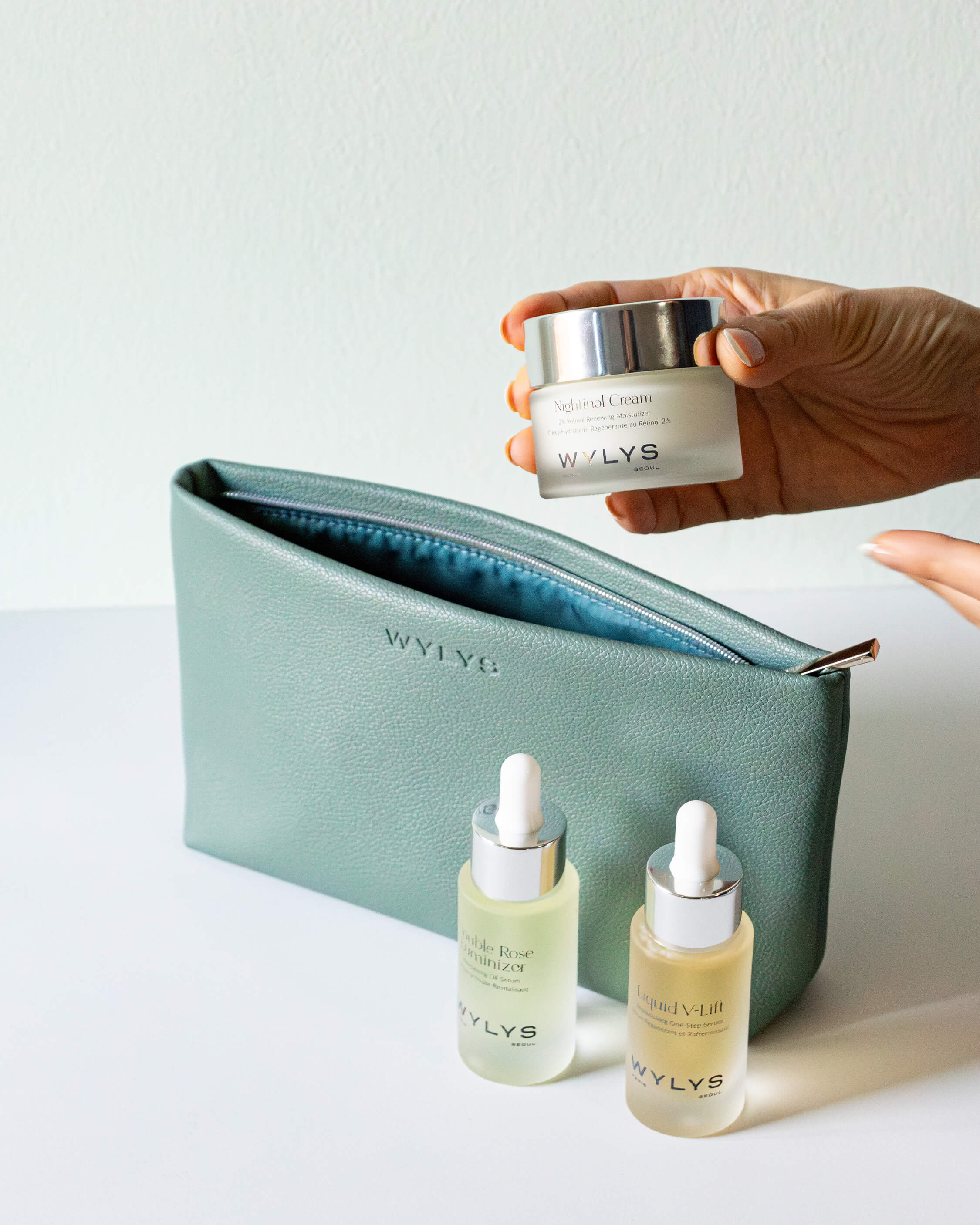 Wylys Sage Verte Makeup Bag – Soft Vegan Leather Pouch for Skincare & Makeup, Metal Zipper & Water-resistant fabric Lining, Hand placing skincare into bag.