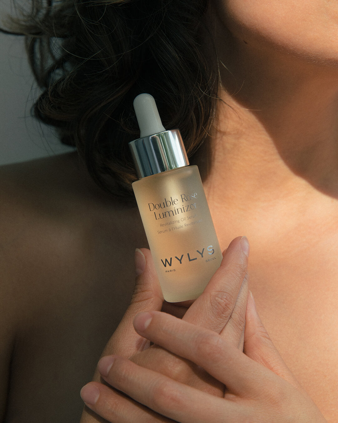 WYLYS Double Rose Luminizer When You Love Your Skin Model holding bottle in hand. Luxury vegan cruelty free oil blend made in France. Multipurpose oil, serum, makeup booster in one. Organic ingredients. Clean beauty.