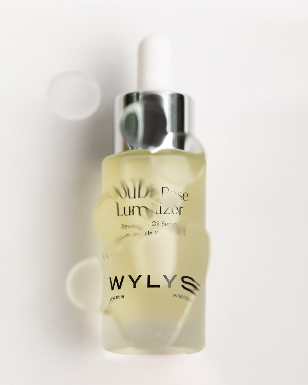 WYLYS Double Rose Luminizer Texture When You Love Your Skin. Oil over bottle, distorted printing on bottle. Stylized image. Oil. Luxury. Made in France. Vegan. Cruelty free. Organic.