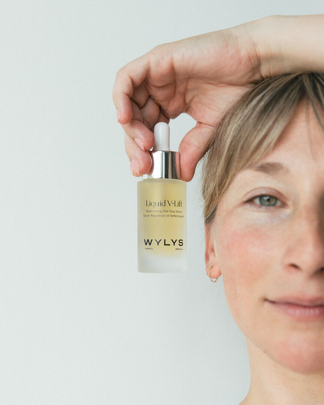 Ohlolly Korean Skincare Wylys Liquid V-Lift, WYLYS Liquid V-Lift – Peptide-infused lifting serum with AFA-GS Alga Complex to firm, hydrate, and smooth fine lines for youthful skin. Made in France. Model holding Bottle.