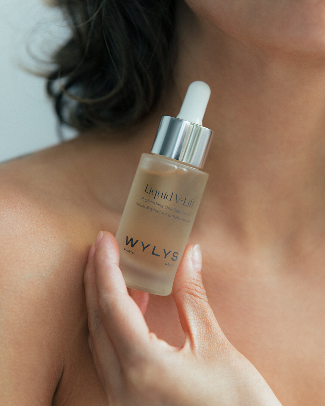 Ohlolly Korean Skincare Wylys Liquid V-Lift, WYLYS Liquid V-Lift – Peptide-infused lifting serum with AFA-GS Alga Complex to firm, hydrate, and smooth fine lines for youthful skin. Model holding bottle close to body.