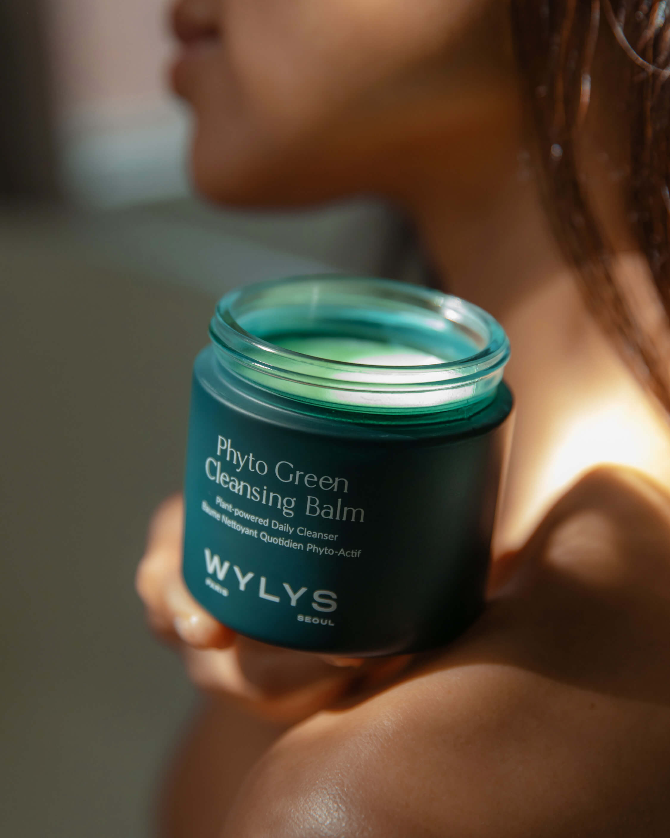 WYLYS Phyto Green Cleansing Balm – Luxurious balm-to-oil cleanser. Model holding open jar to show size, color, texture.