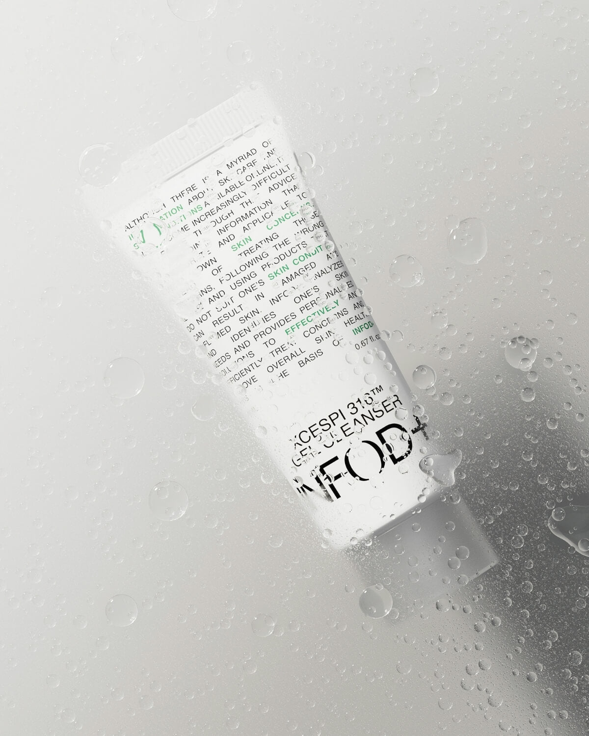 Close-up of the small INFOD+ XCESPI 316™ Gel Cleanser tube lying flat and covered in droplets of water.