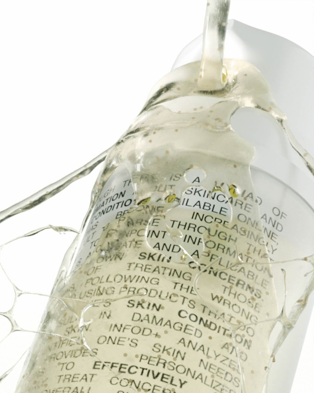 Extreme close-up of clear, yellowish gel cleanser dripping over the label of the INFOD+ bottle, showing its thick texture.