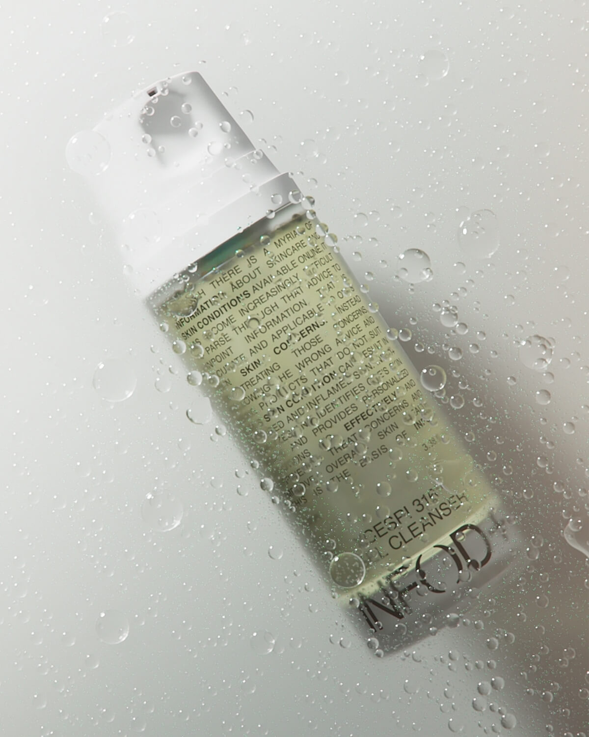 The INFOD+ XCESPI 316™ Gel Cleanser bottle, covered in droplets of water and tilted against a bright white background.