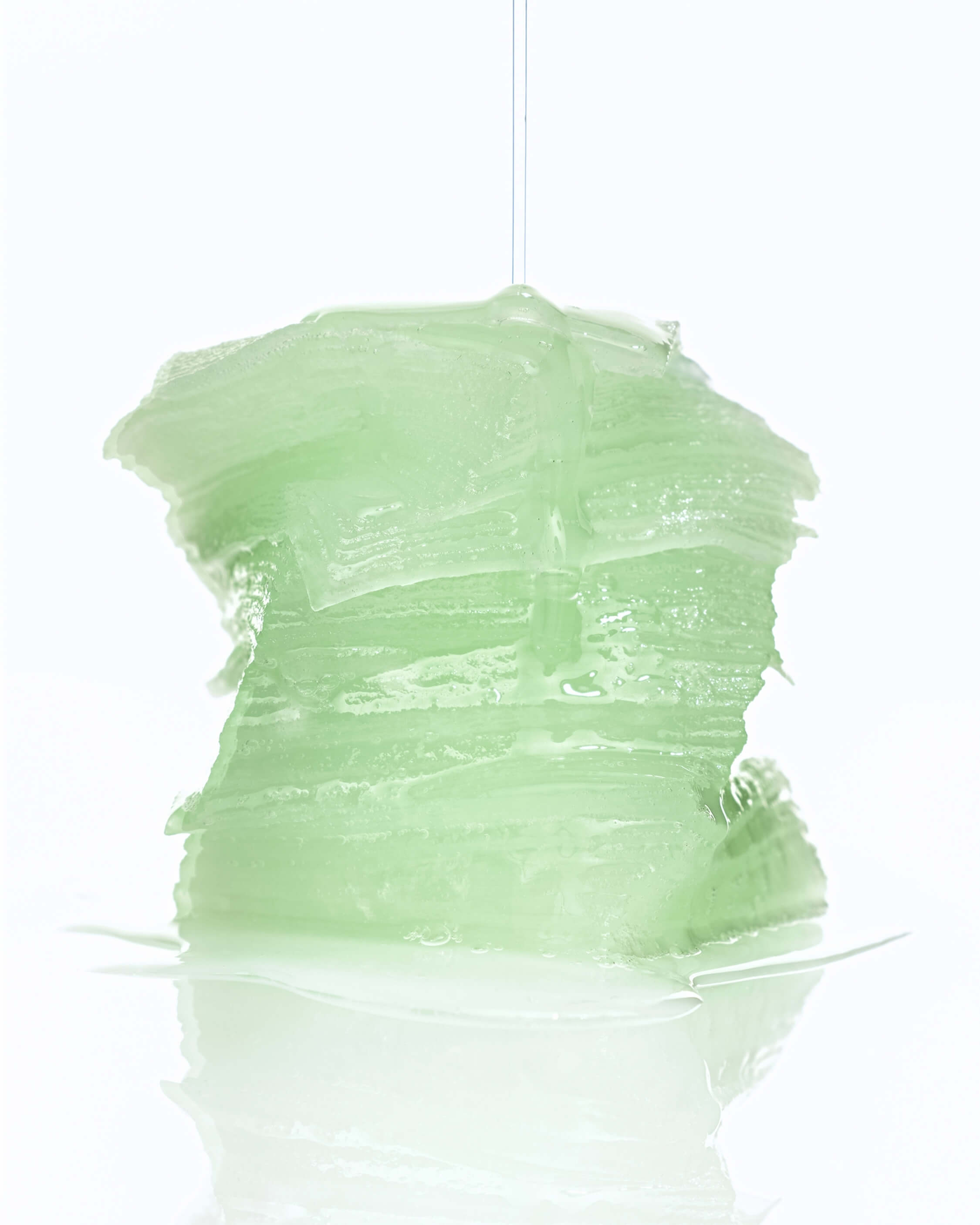 A stack of thick, wavy, light green gel pads is piled high, with liquid dripping from the top.