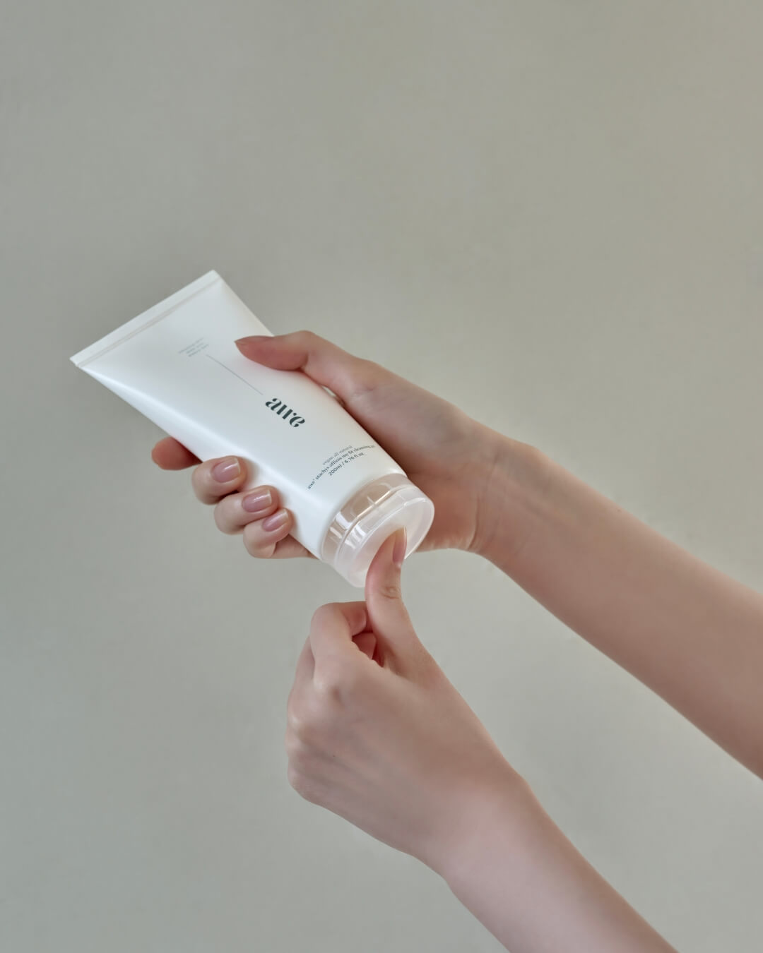 Woman's hands holding an Awe daily cleansing gel tube and opening the flip-top cap.