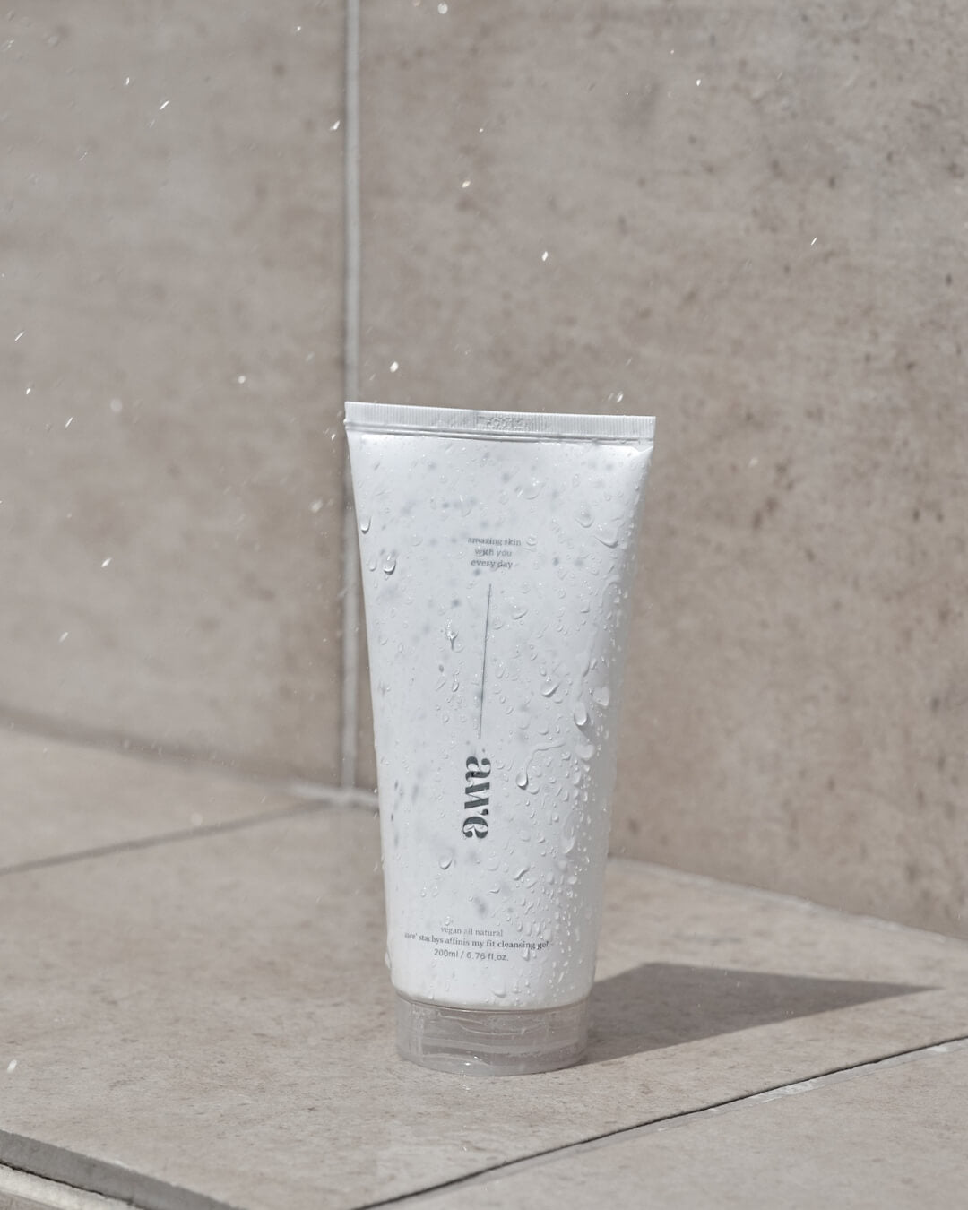 Water droplets splashing onto an Awe facial cleansing gel tube on outdoor stone tile.