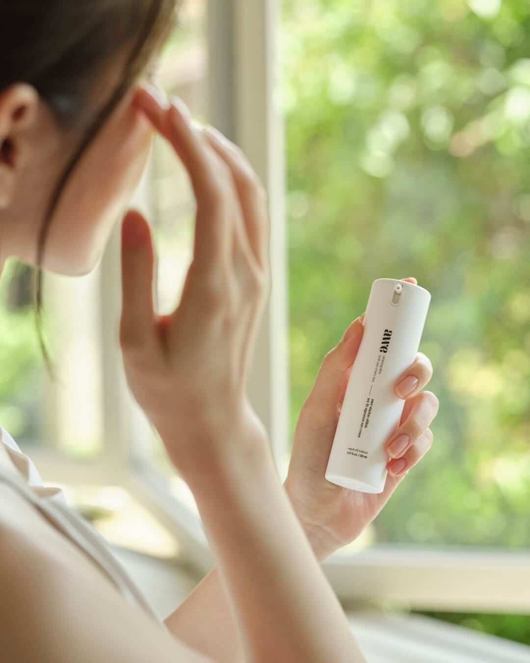 Woman holding an Awe daily eye cream bottle while gently applying product near her eye.