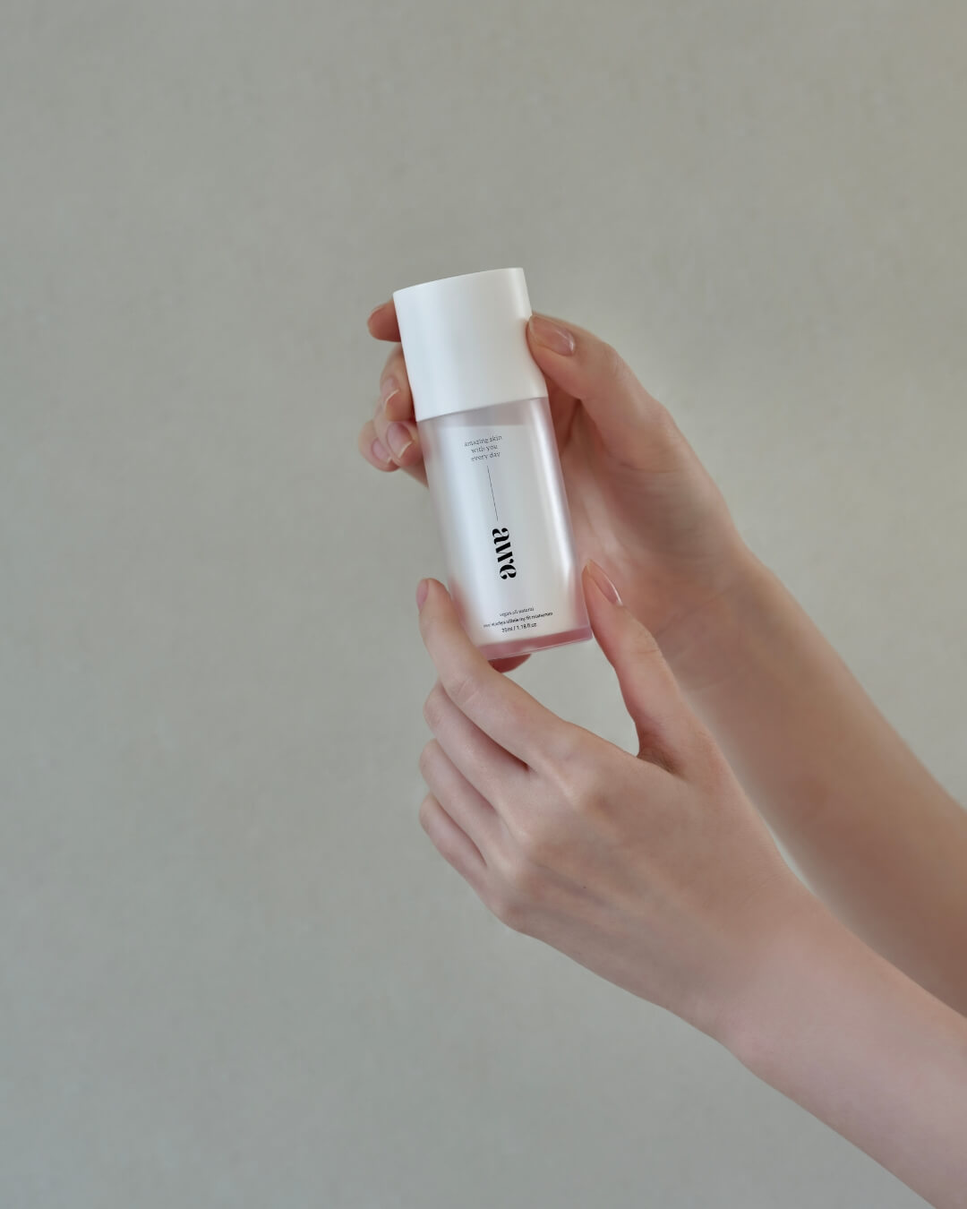 Close-up of a woman’s hands gently holding a bottle of Awe firming face mist serum.