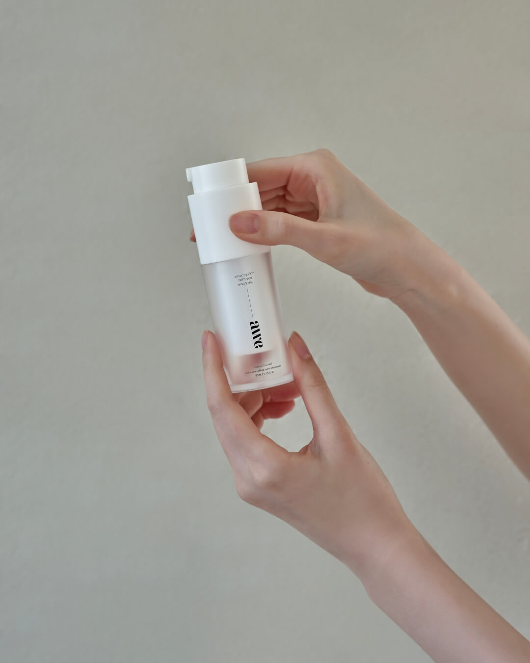 Close-up of hands holding a bottle of Awe vegan natural firming mist serum against a neutral background.