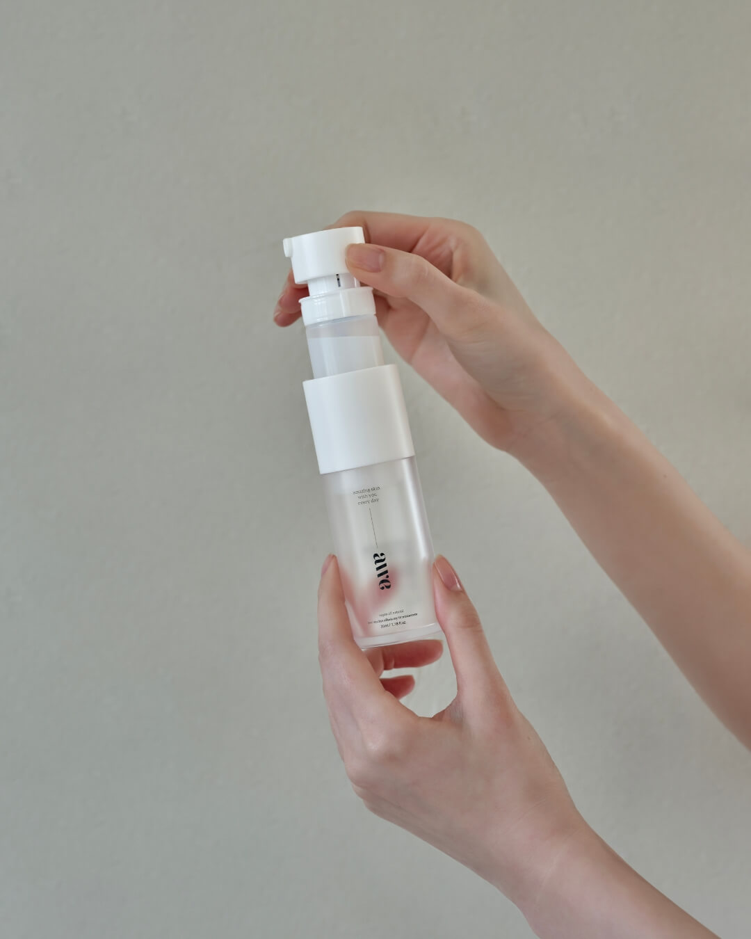 Hands holding and opening the innovative spray pump mechanism of an Awe firming face mist serum bottle.