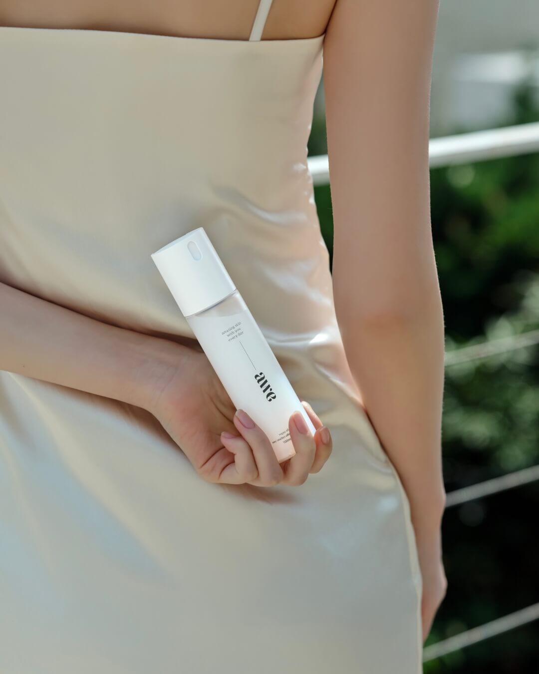 Woman holding an Awe facial firming mist serum bottle behind her back in a satin dress.