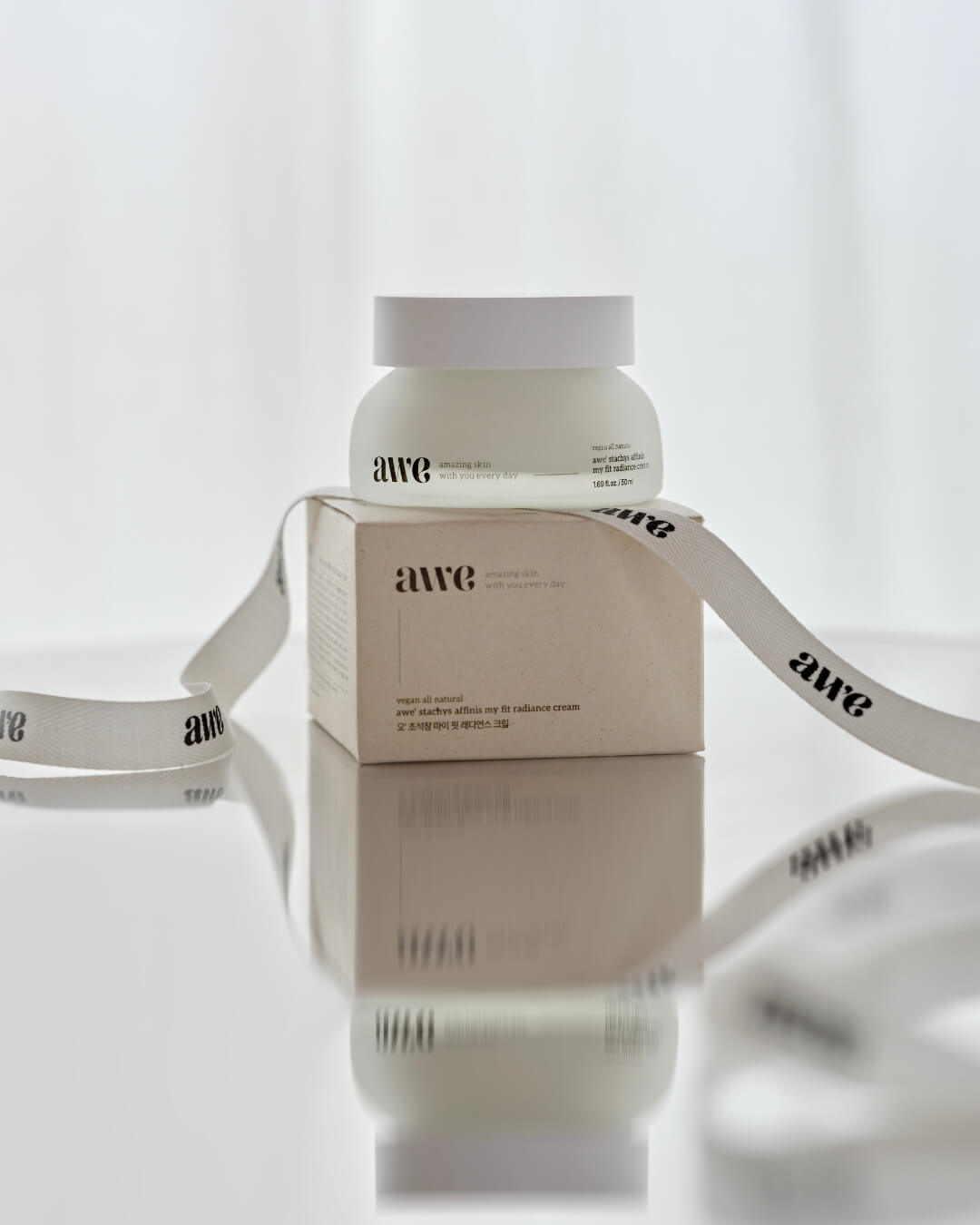 Awe radiance cream jar sitting on its product box wrapped with a branded white ribbon.