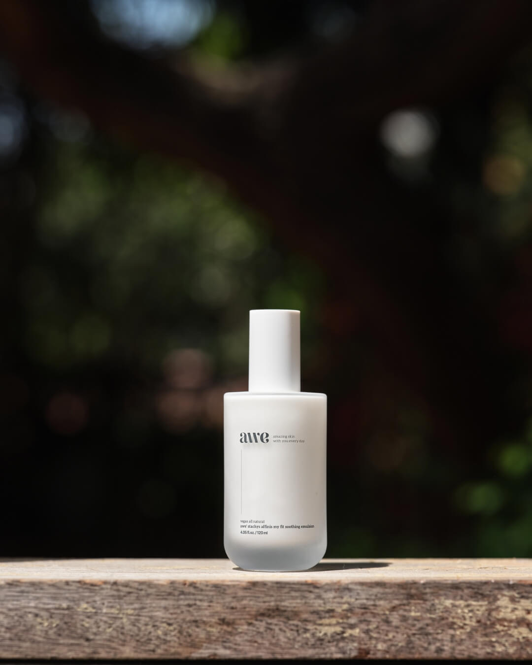 Awe natural soothing emulsion pump bottle placed on an outdoor wooden surface.