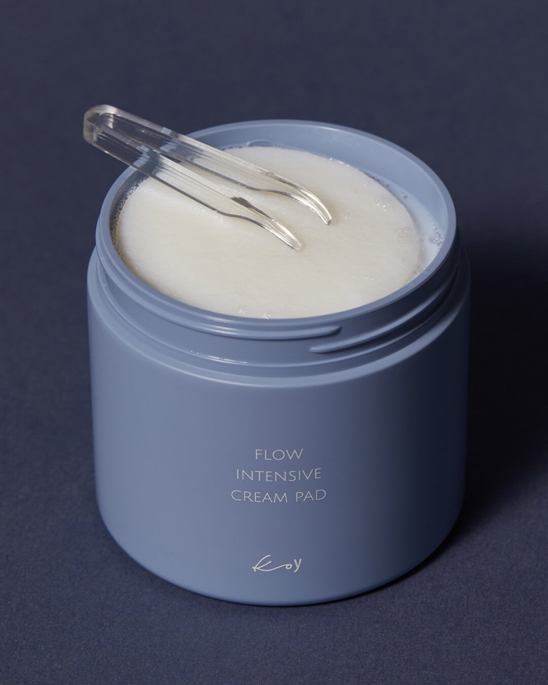 Open jar of koy Flow Intensive Cream Pads filled with round white facial cotton pads and clear skincare tweezers.
