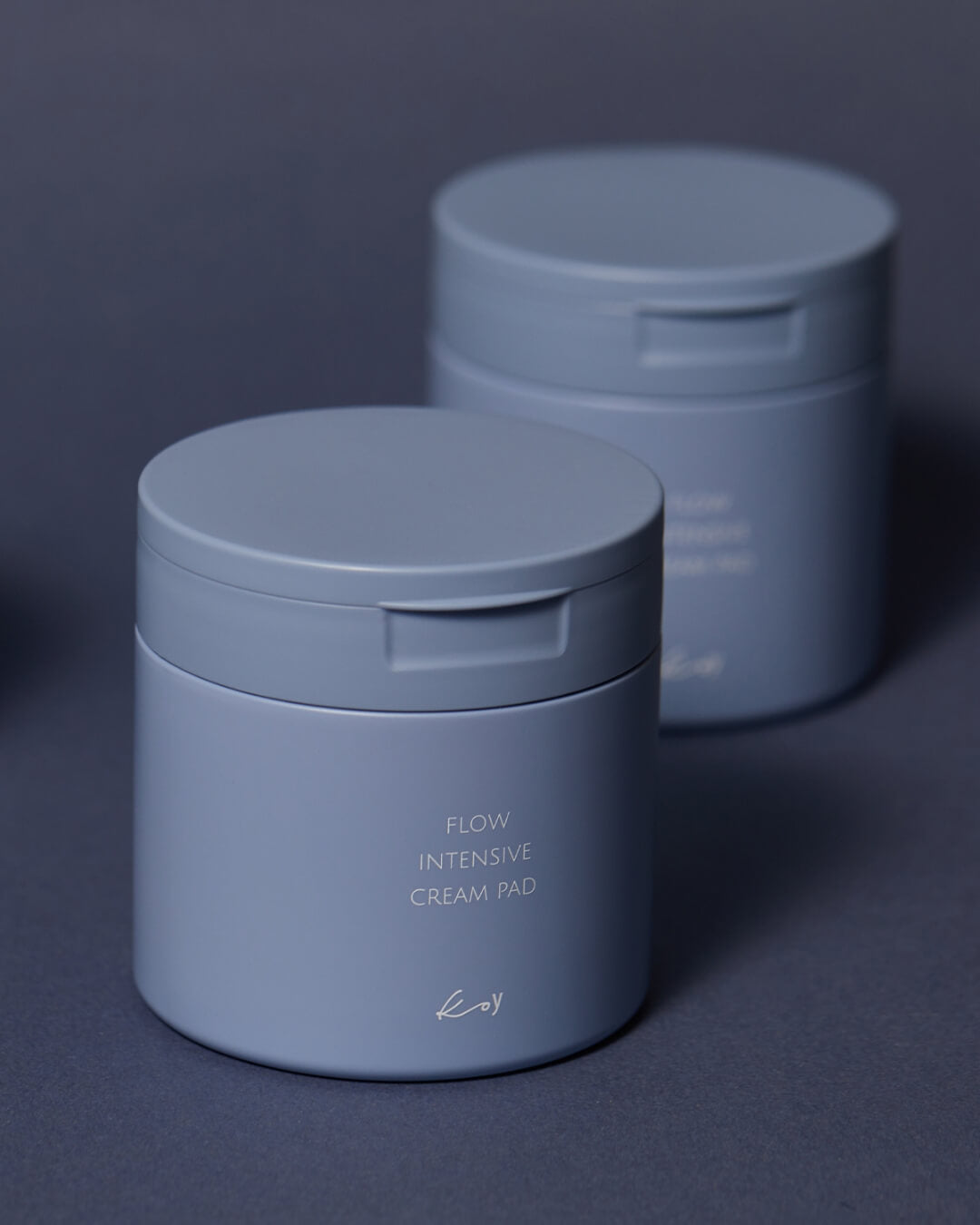 Two closed blue containers of koy Flow Intensive Cream Pad on a dark blue background.