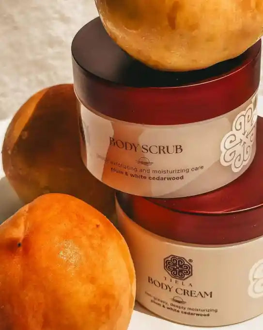 Two jars of body scrub and cream with peaches on a textured surface