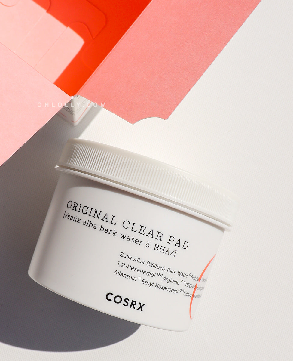 Cosrx One Step Original Clear Pad Cosrx Original Clear Pad tub with BHA and Willow Bark Water ingredients, next to its packaging on an orange background.