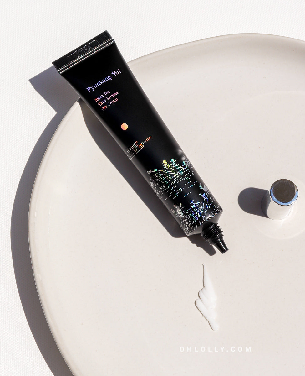 Overhead studio shot of the black Pyunkang Yul Black Tea Time Reverse Eye Cream tube lying diagonally on a pale pink porcelain dish. A rich dollop of the white cream is visible next to the tube's nozzle, emphasizing its lightweight, creamy, and anti-aging texture.