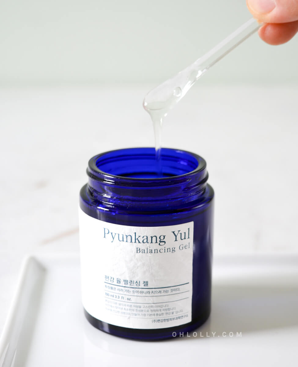 Extreme close-up studio shot of the dark blue Pyunkang Yul Balancing Gel jar with the lid off. A clear plastic spatula is scooping up the thick, honey-like gel, emphasizing its unique, slow-moving texture and concentrated formula.