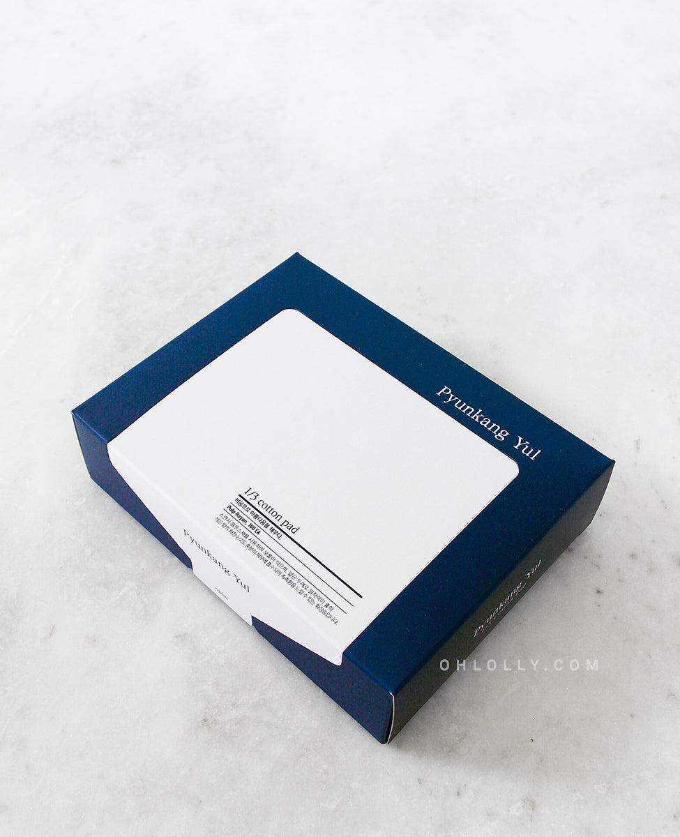 Overhead studio shot of the dark blue Pyunkang Yul 1/3 Cotton Pads box, angled to show the white label with product details on a white, marble-like background.