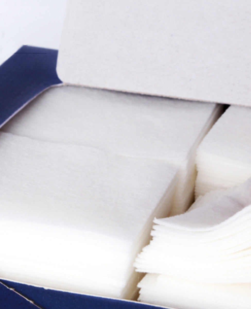 Close-up studio shot of the white, thin, rectangular Pyunkang Yul 1/3 Cotton Pads stacked next to their dark blue box, highlighting the pads' smooth texture and thin design, which helps save on toner and essence.